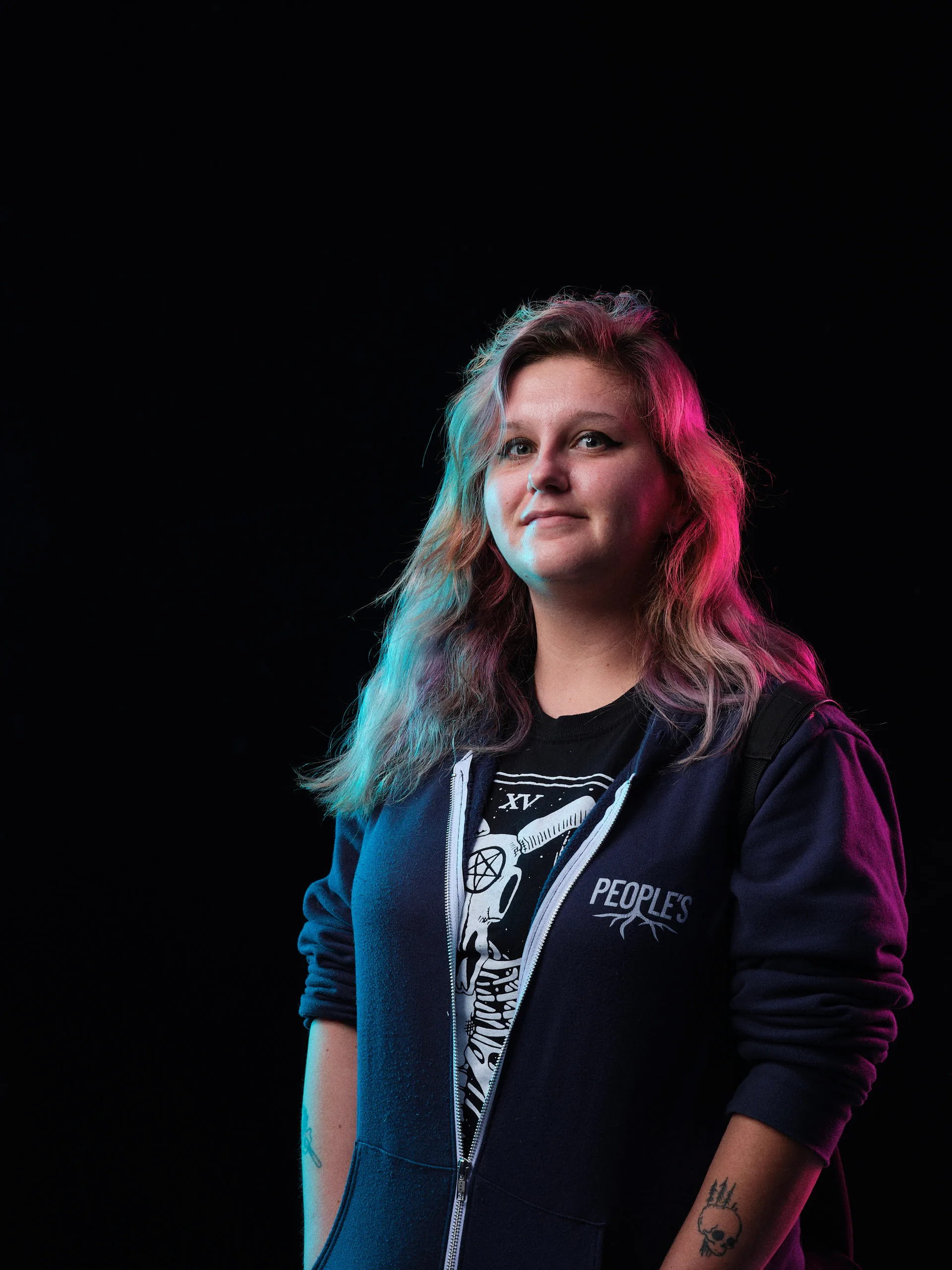 Character portrait of a woman in a blue zip-up hoodie, featuring vibrant magenta and cyan rim lighting against a dark background, high-fidelity GFX medium format capture.