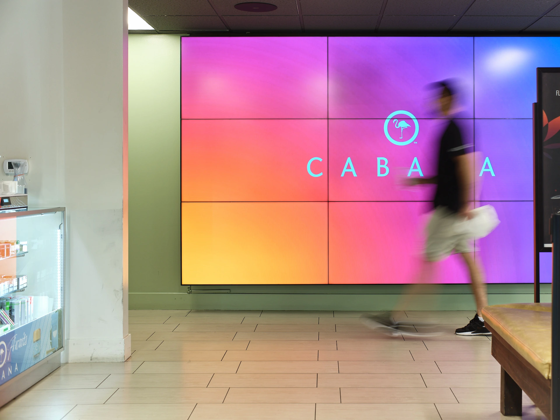 Long exposure interior photography of a modern Los Angeles retail space featuring a blurred patron in motion against a vibrant magenta and orange digital display wall, captured on GFX.