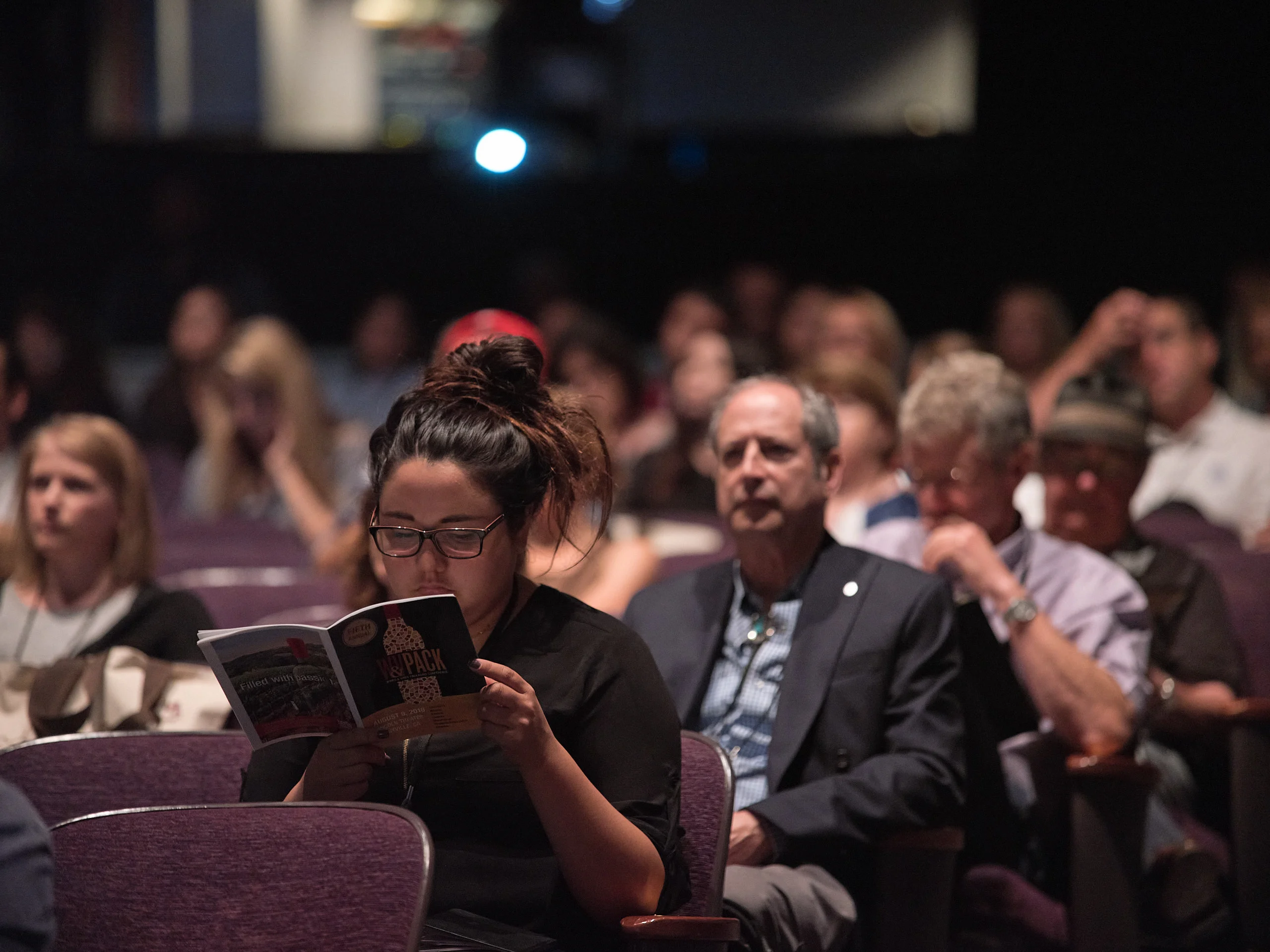 Institutional documentation by San Francisco photographer; an attendee reviewing a program during a presentation at a Napa wine industry conference, captured on GFX with shallow depth of field.